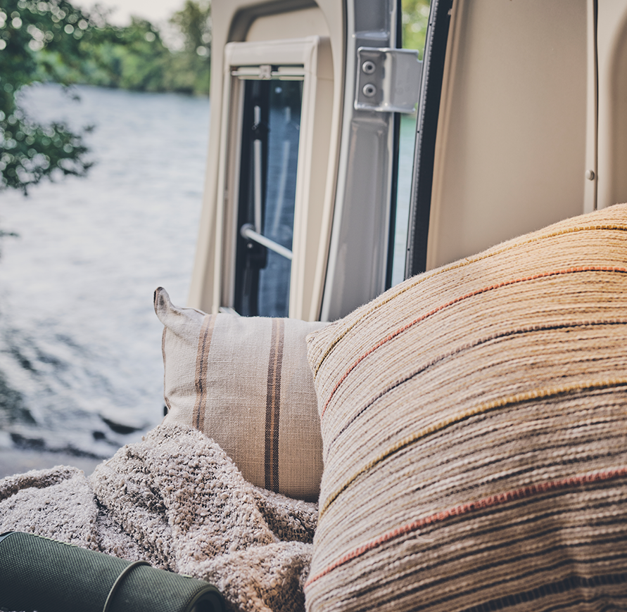 Sunlight CLIFF 600 Adventure mit Schlafbereich, Blick durch die Hecktüre auf Fluss, kuschlige Decken und Kissen, Musikbox